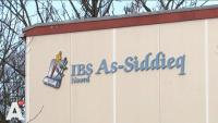 Bewegwijzering voor "ibs as-siddieq noord" met een logo op de zijkant van een gebouw.