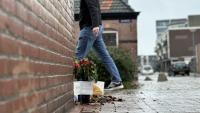 Een man laat bloemen achter op een bakstenen muur.