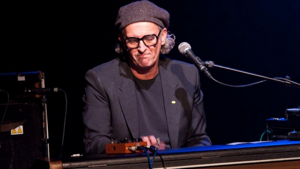 Een man met een hoed en een bril speelt op een toetsenbord.