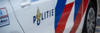 Een close-up van de deur van een Nederlandse politieauto met het logo "POLITIE", vergezeld van een vlammend fakkelembleem. De auto is voorzien van blauwe en rode diagonale strepen. Het witte oppervlak van de auto is ook gedeeltelijk zichtbaar.