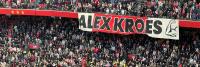 Groot spandoek met de tekst "alex kroes" opgehouden door enthousiaste voetbalfans in een druk stadiongedeelte.