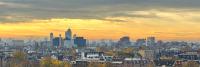 Een panoramisch uitzicht over Amsterdam bij zonsondergang, met een levendige hemel boven de traditionele architectuur van de stad, moderne gebouwen en grachten vol met boten.