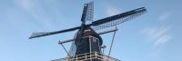 Een traditionele Nederlandse windmolen tegen een helderblauwe lucht, met een zwart-witte structuur met vier grote wieken.