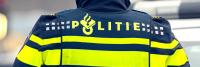 Van achteren wordt een persoon getoond die een politiejasje draagt met het opvallende opschrift "POLITIE" op de achterkant. De jas heeft goed zichtbare gele strepen met reflecterende eigenschappen en een symbool boven de tekst.