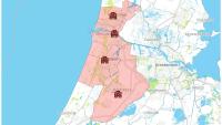 Een kaart die een roze gearceerde regio markeert die delen van Noord-Holland omvat, waaronder steden Amsterdam, Haarlem en Hoofddorp. Rode vierkante iconen met zwarte patronen markeren specifieke locaties binnen het gearceerde gebied. Nabijgelegen steden 