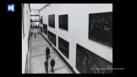 Een zwart-witfoto van een gang van een kunstgalerie met verschillende grote ingelijste schilderijen aan de muren. Een paar mensen lopen en staan in de gang. De gang heeft een hoog plafond met natuurlijk licht dat er doorheen komt.