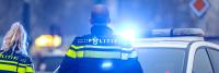 Twee politieagenten in uniform staan bij een politieauto met zwaailichten. De scène lijkt zich in een stedelijke omgeving af te spelen en de agenten kijken weg van de camera. Op de politieauto staat "Politie".